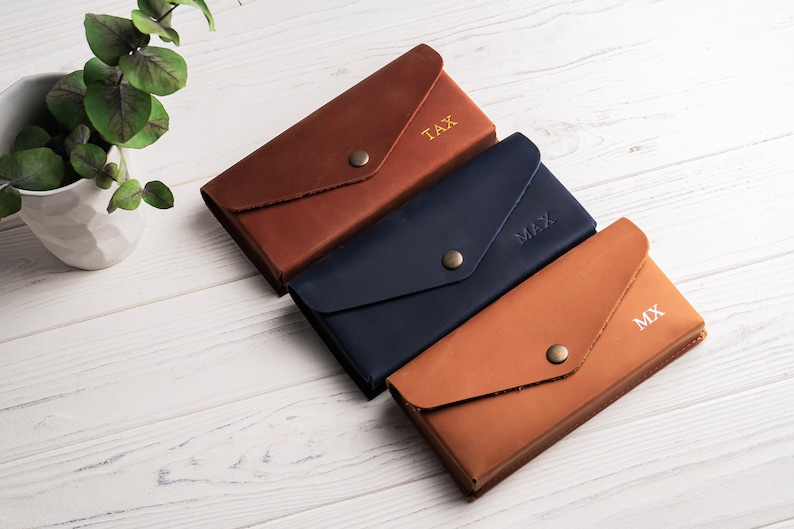 May include: Three leather wallets in brown, blue, and brown with gold lettering. The wallets are personalized with the initials "TAX", "MAX", and "MX".