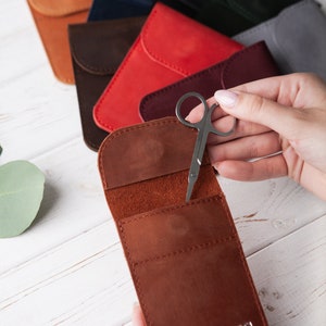 May include: A brown leather case with a flap that opens to reveal a small pair of silver scissors. The case has a single initial, "UC", embossed on the front.