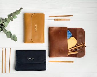 May include: Two leather cases for knitting needles, one brown and one blue, with the names "ALYSON" and "DOLIE" printed on them. The brown case is open and contains a variety of knitting needles and yarn.