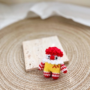 May include: A crocheted clown doll with a red and white striped outfit, yellow body, and red hair. The doll is sitting on a woven straw mat.