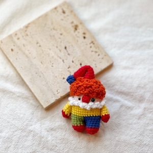 May include: A crocheted clown doll with red hair, a yellow shirt, green and blue pants, and red shoes.