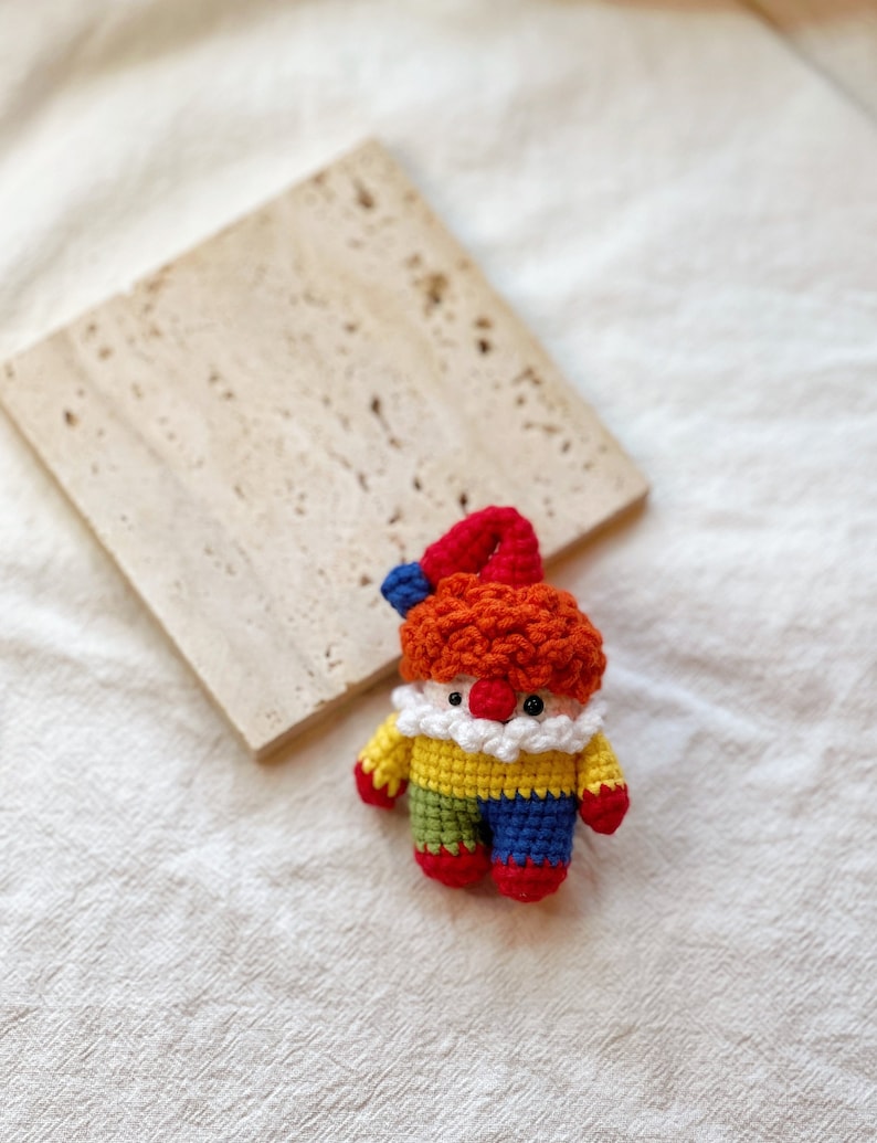 May include: A crocheted clown doll with red hair, a yellow shirt, green and blue pants, and red shoes.