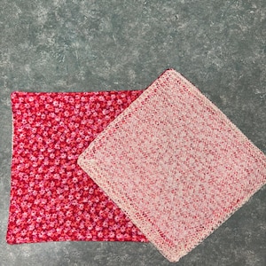 May include: Two square fabric items. One is a vibrant red with a small floral pattern. The other is a light pink with a woven texture. Additional blue and navy blue fabric items are visible in the background.