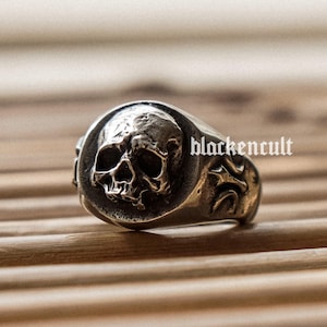 May include: A silver ring with a skull design. The skull is detailed and has a prominent nose and eye sockets.