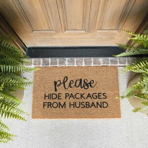 May include: A brown coir doormat with the text "Please hide packages from husband" in black lettering.