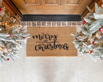 May include: A brown coir doormat with the text "merry christmas" in black cursive lettering.
