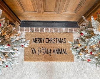 May include: A brown coir doormat with the text "Merry Christmas Ya Filthy Animal" in black lettering.