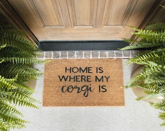 May include: A brown coir doormat with the text "Home is where my corgi is" in black lettering.