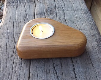 May include: A wooden candle holder with a triangular shape and a metal insert for a tea light candle. The candle is lit and the holder is sitting on a wooden surface.