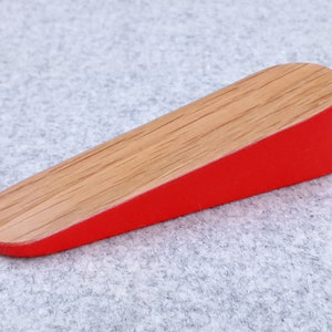 May include: A wooden doorstop with a red painted bottom and a natural wood top.