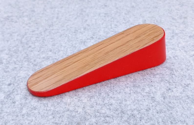 May include: A wooden doorstop with a red painted bottom and a natural wood top.