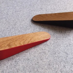 May include: Two wooden door stops, one with a red base and one with a black base. Both have a natural wood finish on the top.