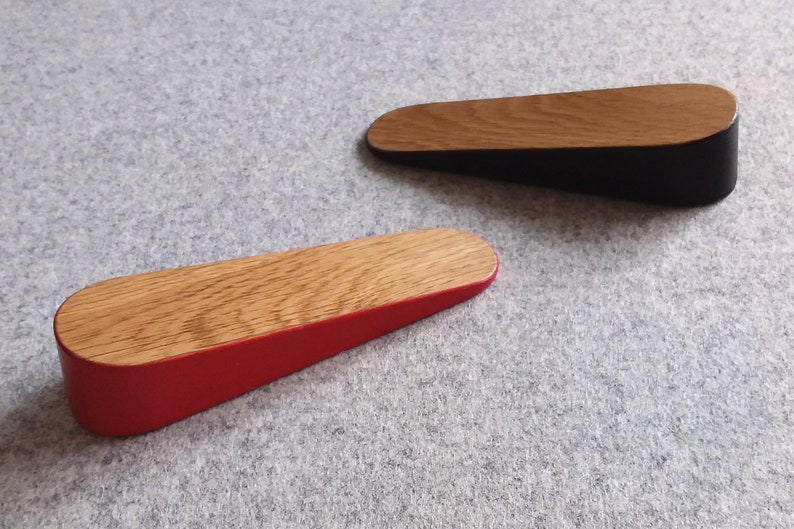 May include: Two wooden door stops, one with a red base and one with a black base. Both have a natural wood finish on the top.