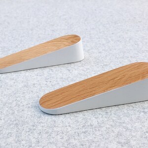 May include: Two white door stops with a wood top. The door stops are shaped like a wedge.