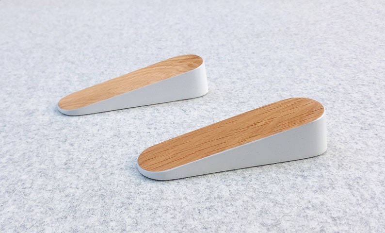 May include: Two white door stops with a wood top. The door stops are shaped like a wedge.