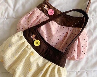 Peut inclure: Deux petits sacs à main en tissu faits à la main. L'un est rose à pois noirs, l'autre est jaune avec un petit motif floral. Les deux ont des accents, des anses et des boutons décoratifs marron.