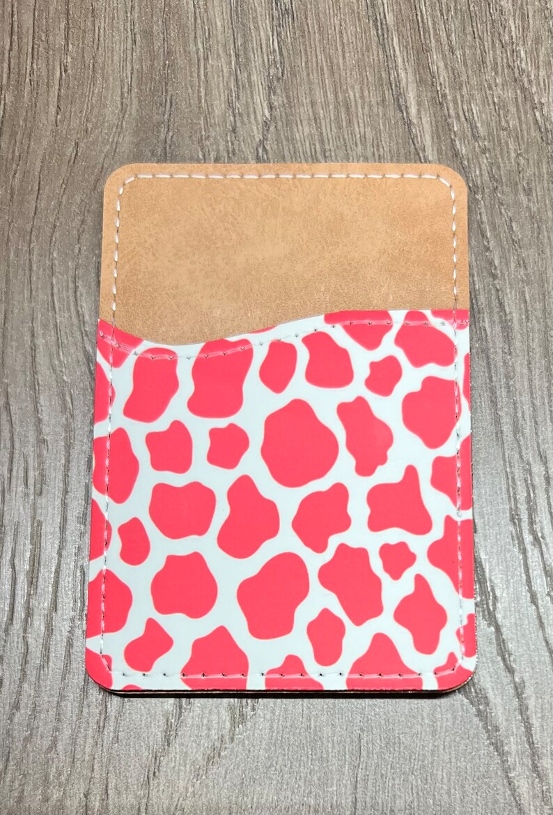 May include: A rectangular phone card holder with a light brown interior and a coral and white cow print exterior. The edges are stitched with white thread.
