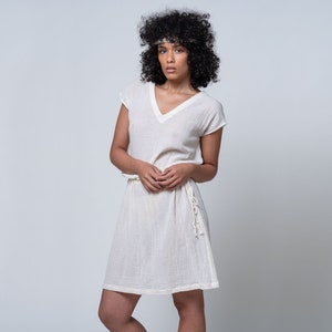 Peut inclure: Une robe blanche à manches courtes et à col en V avec une ceinture à nouer à la taille. La robe est faite d'un tissu léger et fluide. Le mannequin porte un bandeau.