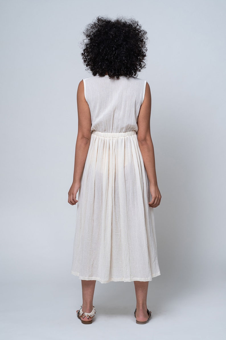 K&ouml;nnte beinhalten: Ein wei&szlig;es, &auml;rmelloses Kleid mit geraffter Taille und einem flie&szlig;enden Rock. Das Kleid ist aus einem leichten Stoff gefertigt und hat eine lockere Passform.