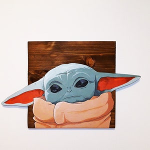 Peut inclure: Une enseigne en bois peinte à la main représentant un personnage extraterrestre vert de dessin animé avec de grandes oreilles, portant une robe brune. Le personnage a de grands yeux et une expression sérieuse.