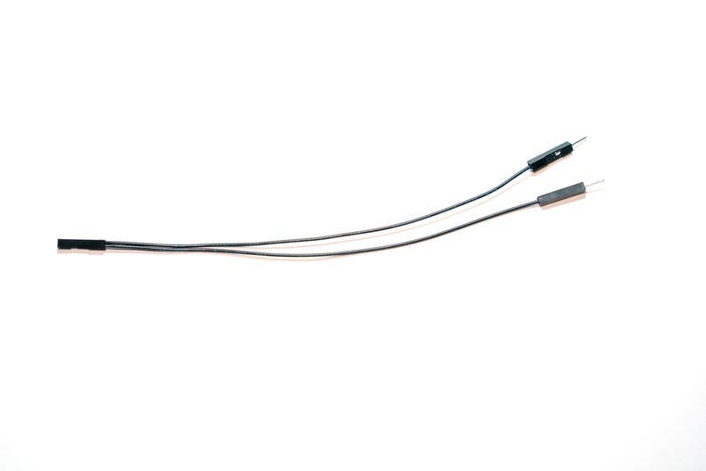 May include: Two black jumper wires with female connectors on one end and male pin connectors on the other. The wires are thin, flexible, and black in color, featuring rectangular plastic housings at the connection points for electronic components.