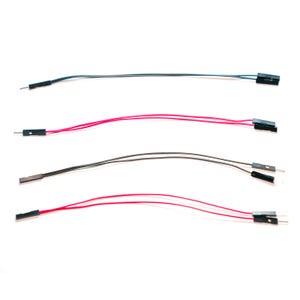 May include: Four jumper wires arranged horizontally. Each wire features a flexible insulated cord in either black or red, with a black plastic connector housing at both ends. The connectors contain exposed metal pins or sockets for electronic connections.