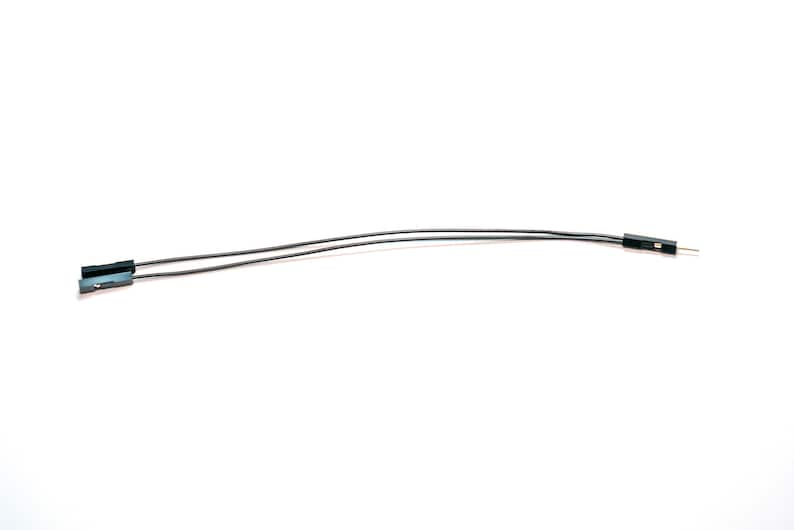 May include: A pair of thin, flexible black electrical jumper wires. Each wire features a small black plastic connector housing at one end, while the other end terminates in a single exposed metal pin connector for electronic circuit connections.