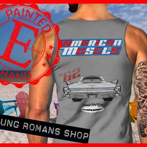 May include: A gray tank top with a vintage car graphic and the text "American Muscle" in blue and red. The car is a white 1962 Cadillac with the text "Howle Hot Rod" below it. The tank top has a distressed red stamp that says "Painted by Hand" in a circle.