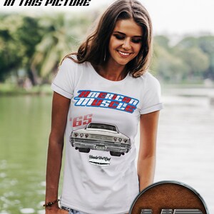 May include: White unisex t-shirt with a vintage car graphic and the text "American Muscle" and "65" printed on the front. The car is a silver 1965 Chevrolet Impala. The sleeves are rolled up. The text "Hoola Hot Rod" is printed below the car graphic.