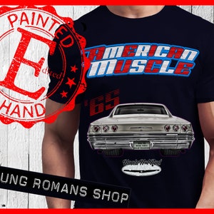 May include: A navy blue t-shirt with a white and red "American Muscle" graphic, a vintage car illustration, and the text "Painted by Hand" in a red circle stamp. The car is a white 1965 Chevrolet Impala with the text "Wide Tires Solid Bearing" and "Woodie Hot Rod" on the back.
