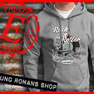 以下が含まれることがあります： 「Rock 'n' Roller」の文字と、ビンテージのマイク、車、レコードプレーヤーのグラフィックデザインが施されたグレーのパーカー。「Young Romans Shop」の文字も含まれています。