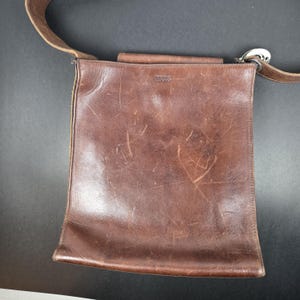 Bolsa de couro da marca ROOTS, estilo carteiro com fecho magnético interno, em condições vintage, design em couro grosso.