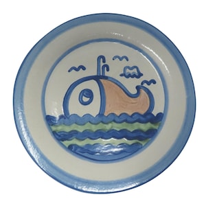 Puede incluir: Un plato de cerámica con un diseño caprichoso. El plato presenta un borde azul y blanco, que rodea una ilustración central de una ballena estilizada en tonos azules y melocotón, con olas y nubes azules. Una pieza encantadora para la decoración de la cocina.