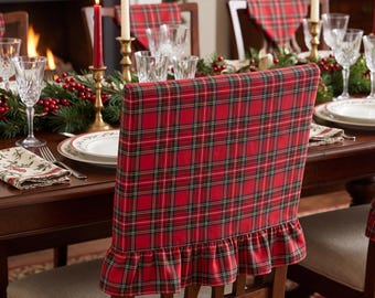 May include: A red, green, and white tartan fabric chair cover featuring a ruffled bottom edge. The cover is designed to fit over the back of a dining chair, displaying a classic plaid pattern with a gathered skirt detail at the base.