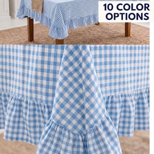 Puede incluir: Un mantel a cuadros vichy en azul claro y blanco con un borde con volantes. La tela cae sobre los lados de una mesa. Un gráfico rectangular blanco en la esquina superior derecha muestra el texto 10 COLOR OPTIONS.