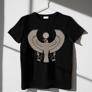 May include: Black t-shirt with a beige graphic print of an Egyptian god with outstretched wings, a sun disc above its head, and two ankh symbols below.
