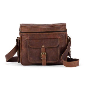 May include: A brown leather messenger bag featuring a rectangular main compartment with a top zipper closure, a front flap pocket secured by a metal buckle strap, and an adjustable shoulder strap attached to the sides with metal hardware.