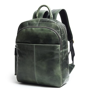 Pode incluir: Uma mochila de couro verde com uma alça superior e alças de ombro ajustáveis. A mochila tem um bolso frontal e um compartimento principal com zíper. O couro tem um acabamento desgastado, dando-lhe um visual vintage. A bolsa é projetada para uso diário.