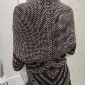 Pode incluir: Um suéter envolvente de malha marrom com um design único. O suéter apresenta um padrão de malha texturizada, um fecho de botão e listras marrons escuras na seção inferior. As mangas também são acentuadas com listras marrons escuras.