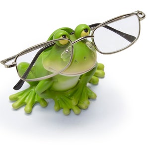 Op de afbeelding: Een groene kikkerfiguur met een zilveren bril. De kikker zit met gekruiste benen en kijkt omhoog.