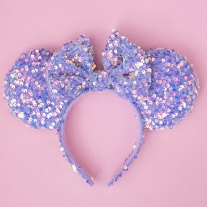 May include: Purple sequined headband with a bow in the center. The headband is shaped like Mickey Mouse ears.