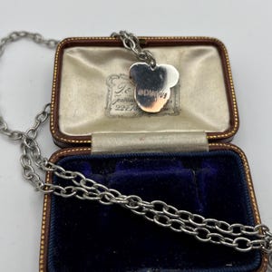 May include: A silver-toned necklace with a Mickey Mouse pendant, displayed in a vintage jewelry box. The pendant features the Disney logo. The box is brown with a blue velvet interior, and the necklace chain is visible.
