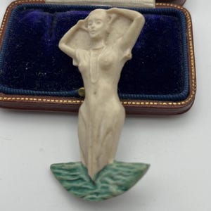 Könnte beinhalten: Eine elfenbeinfarbene Vintage-Figur einer Frau im Wasser mit erhobenen Armen. Die Figur befindet sich in einem blauen Samtinnenraum in einem braunen Etui. Der Sockel ist ein grünes Wellendesign.