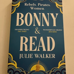 Può includere: Una copertina di libro blu con il titolo "BONNY & READ" di Julie Walker. La copertina presenta un'illustrazione gialla e blu di una nave che naviga sull'oceano.