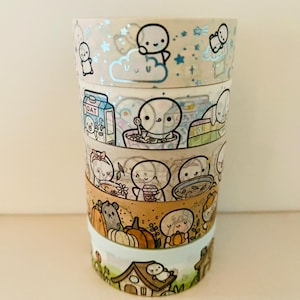May include: A stack of decorative washi tape rolls with cute cartoon characters and themed designs. Designs include a cloud with stars, a bowl of oatmeal, a person with a cup, and a house. The tape is in various colours.