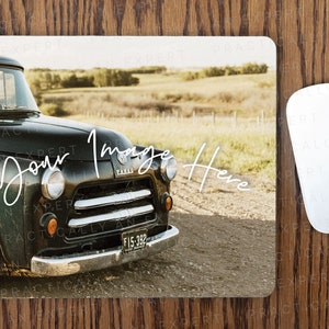 May include: A black vintage pickup truck with a chrome bumper and a license plate that reads "F15-392". The truck is parked on a dirt road with a field of tall grass in the background.