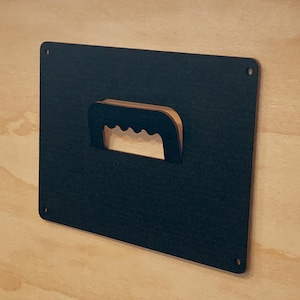 May include: A black rectangular sign with a cut-out handle. The handle is made of a lighter brown material and has a wavy edge.