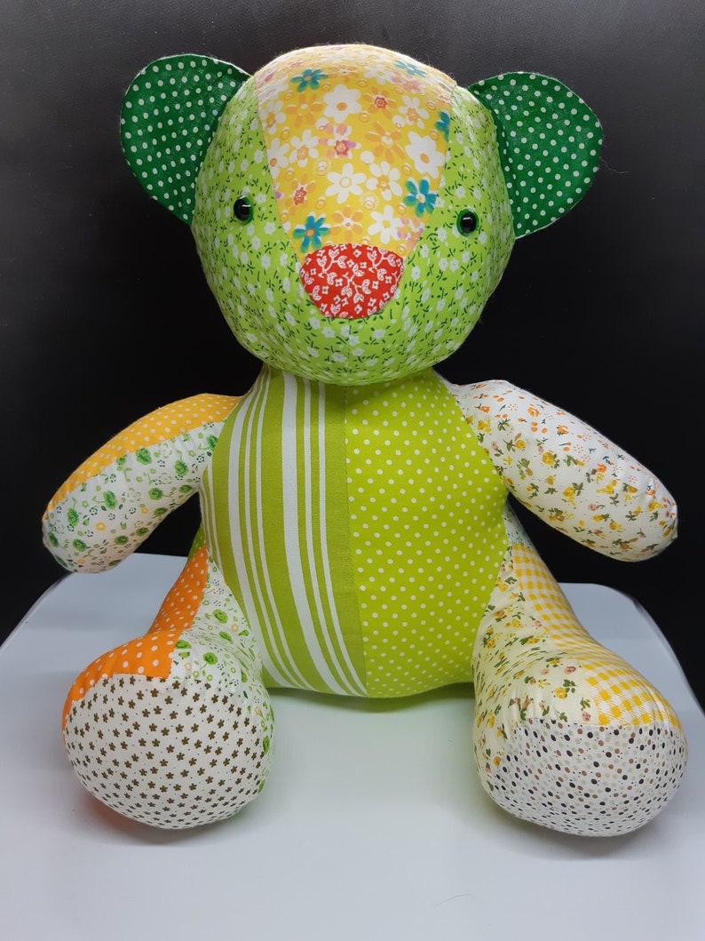 May include: A patchwork green teddy bear made from yellow, orange and white floral fabric. The bear has green ears with white polka dots and black button eyes.