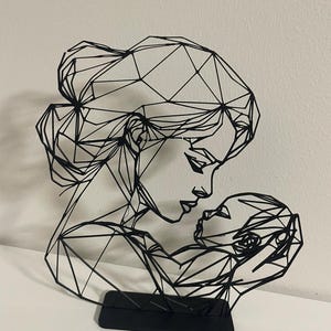 Peut inclure: Sculpture géométrique noire représentant une mère et son enfant. L'œuvre présente un design angulaire stylisé, les formes des figures étant créées par des lignes interconnectées. La sculpture est montée sur un socle rectangulaire noir.