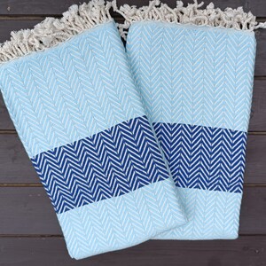 May include: Two blue and white patterned towels with fringe edges. The towels are folded in half and have a chevron pattern.
